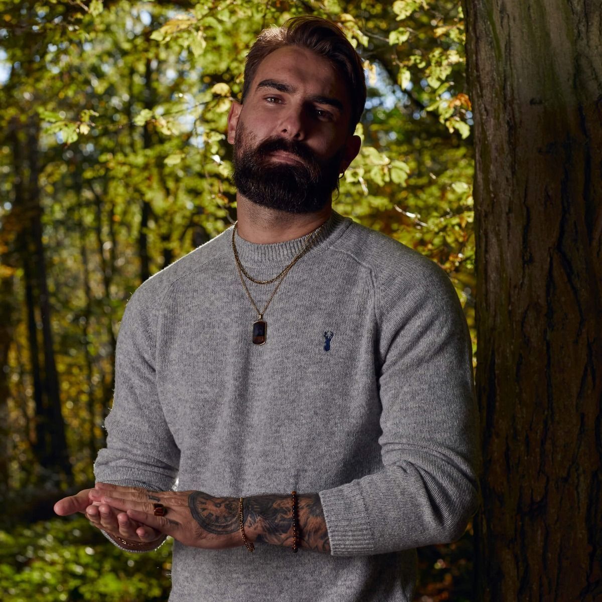 Man wearing Fred Bennett tiger's eye signet ring and matching necklace with grey sweater in forest setting