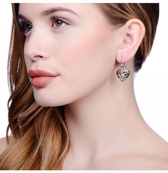 Close-up of a woman wearing sterling silver heart drop earrings by J R Jewellery with wavy brown hair