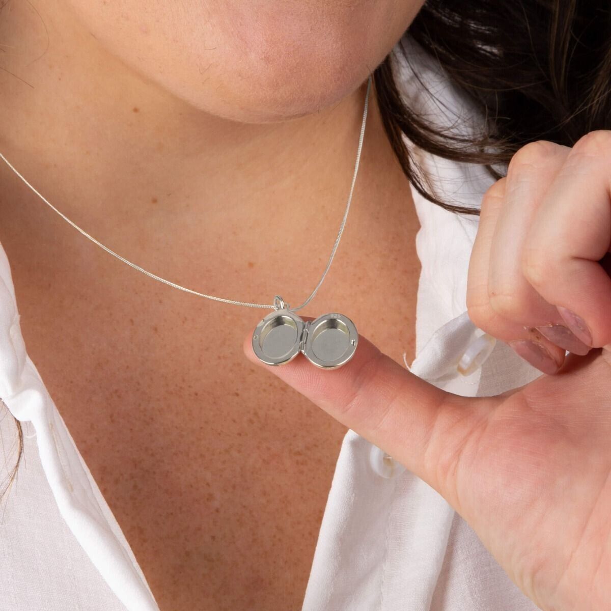 Close-up of sterling silver oval locket pendant worn on a fine chain with the locket open on a person's finger