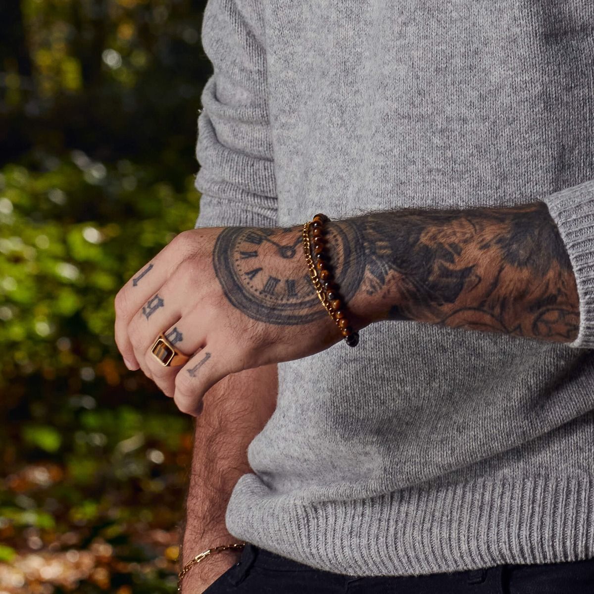 Fred Bennett tiger's eye signet ring worn on finger with tattooed arm and grey sweater background