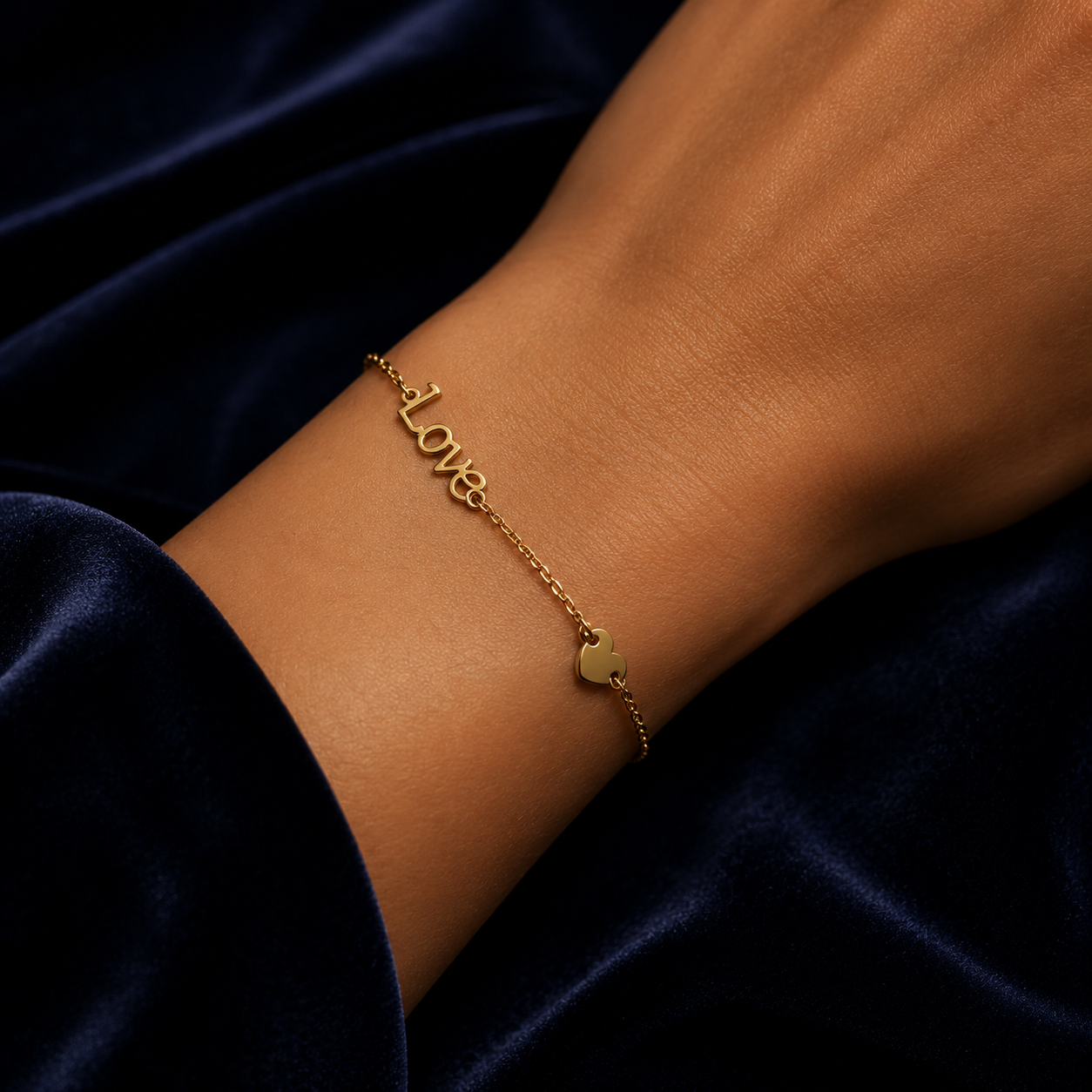 Love Script Bracelet In 9ct Yellow Gold elegantly worn on a wrist against a dark fabric backdrop