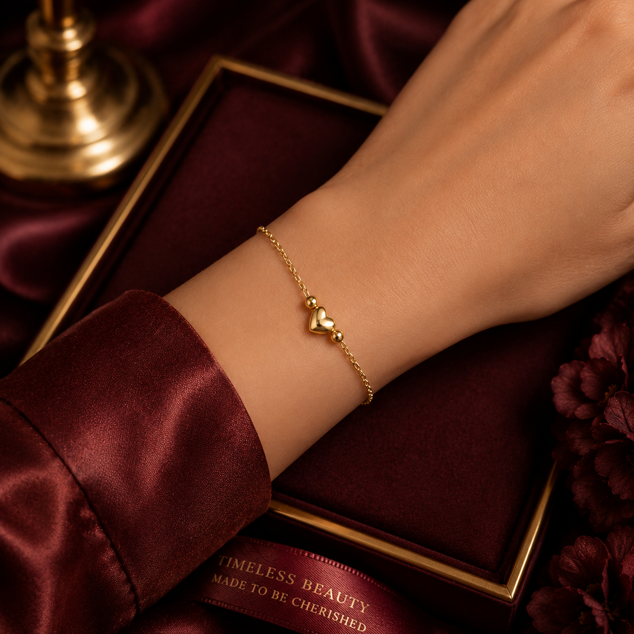 J R Jewellery Minimalist Gold Heart Charm Bracelet worn on a hand against a rich velvet background