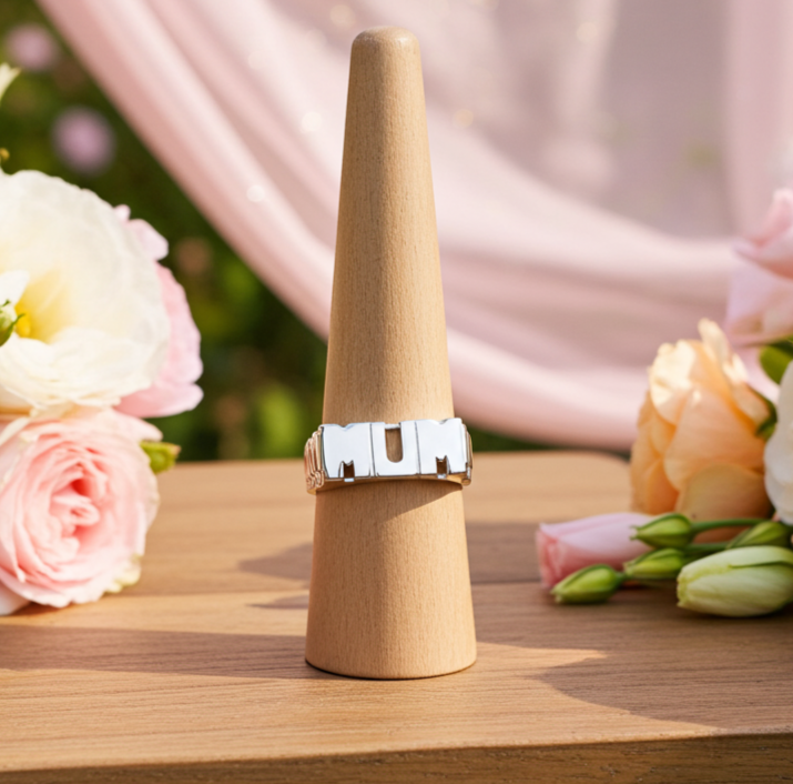 Sterling silver mum ring displayed on a wooden stand surrounded by pink flowers